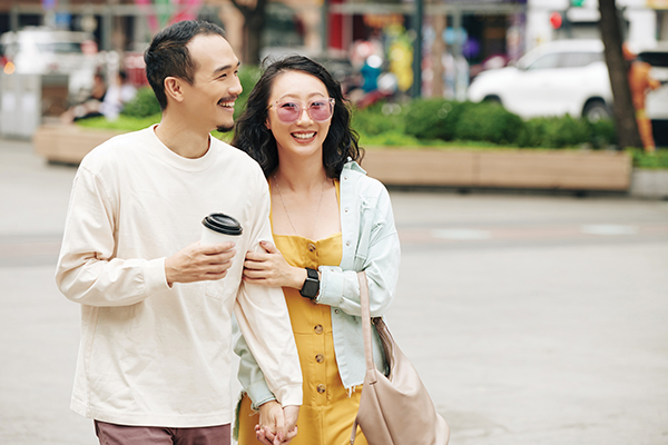 Happy laughing young Chinese couple with take out coffee walking outdoors on windy day