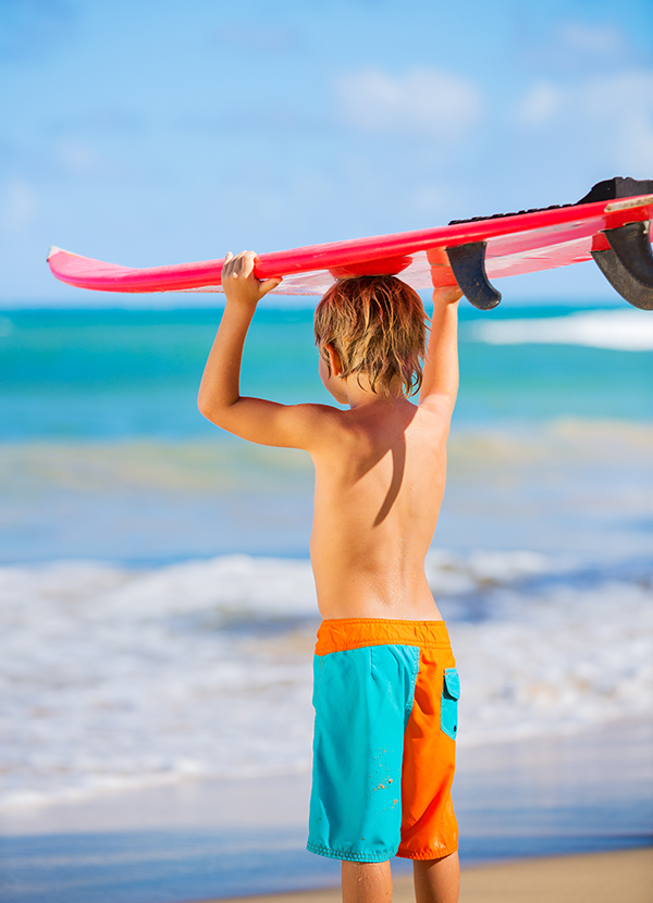 happy young boy at the beach with surfboard
