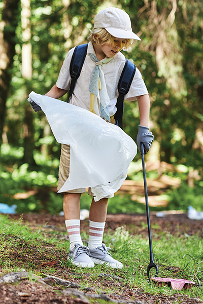 Full length portrait of cute boy as scout helping clean forest during eco awareness field trip, copy space