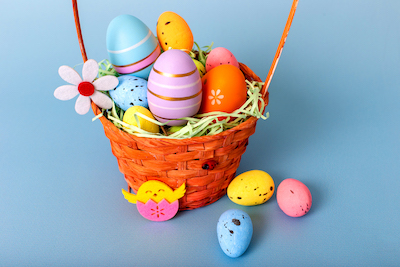 Close up of wicker basket filled with decorative multi colored easters eggs on a light blue background.
