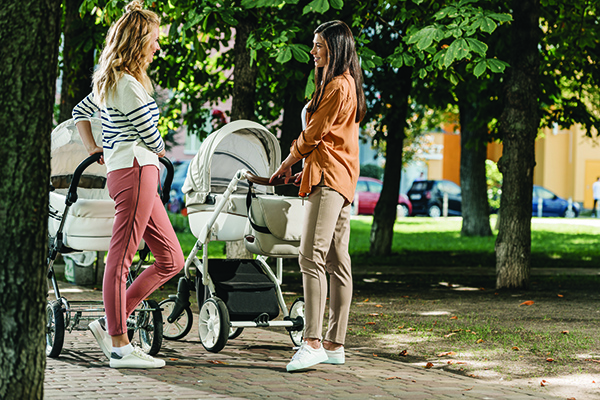 side view of mothers talking and standing with baby strollers in park