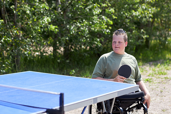 Portrait of young man with disabilty enjoying game of table tennis outdoors, copy space