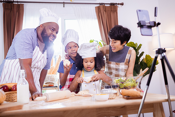 Happy African American family enjoy together with live steam online by smartphone while prepare the flour for making cookies at home