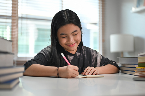 Happy asian teenage woman doing homework at home.