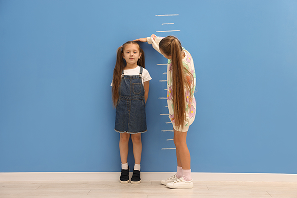 Little girl measuring her friend's height near blue wall indoors